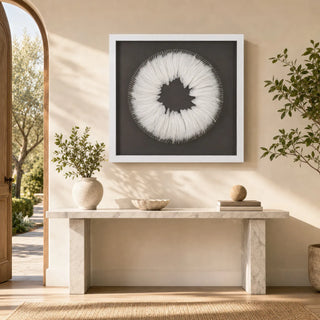 White feather wreath shadow box above a pale stone console in a softly sunlit neutral entryway